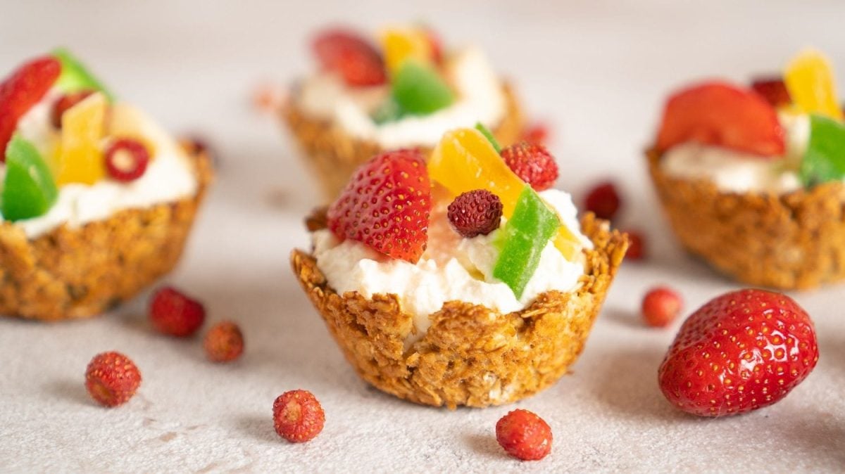 Frontalsicht: Mit Granola-Cuos die mit Joghurt gefüllt und mit frischen Früchten dekoriert sins stehen auf einem hellen Untergrund.