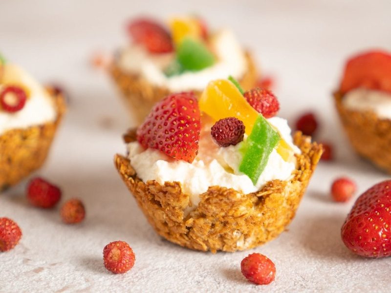 Frontalsicht: Mit Granola-Cuos die mit Joghurt gefüllt und mit frischen Früchten dekoriert sins stehen auf einem hellen Untergrund.