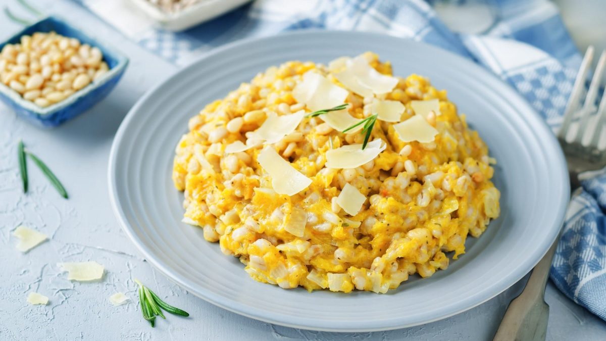 Graupenrisotto mit Kürbis und frisch geriebenem Parmesan, serviert auf einem grauen Teller auf hellem Untergrund.