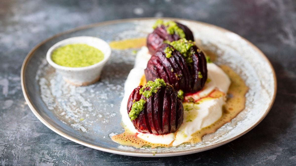 Drei gefächerte Hasselback-Betes auf einem Teller mit grünem Dressing und Jogurt.