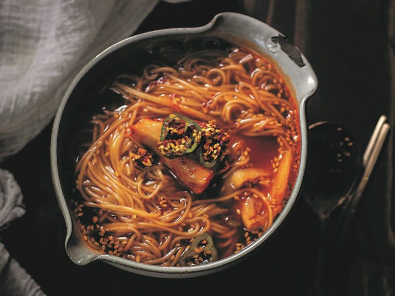 Ein Topf Kimchi-Nudeln mit grünen Chilis in der Draufsicht.