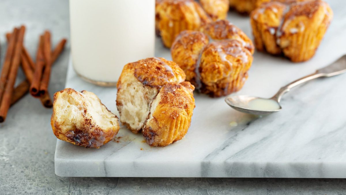 Eine weiße Amrmorplatte mit den Monkey-Bread-Muffins. Im Hintergrund sind unscharf eine Karaffe mit Sahne und ein paar Zimtstangen zu erkennen.