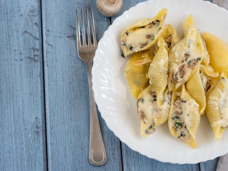Draufblick: Auf einem blauen Untergrund aus Holz steht ein Teller Gefüllte Muschelnudeln mit Gorgonzola und Speck. Daneben liegt eine Gabel.