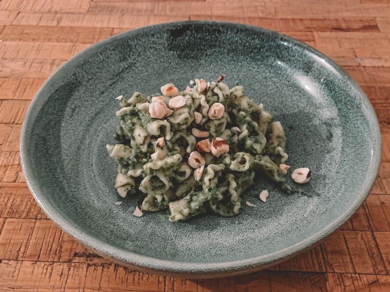 Ein Teller Pasta mit Brokkoli-Grünkohl-Sauce und gehackten Haselnüssen bestreut.