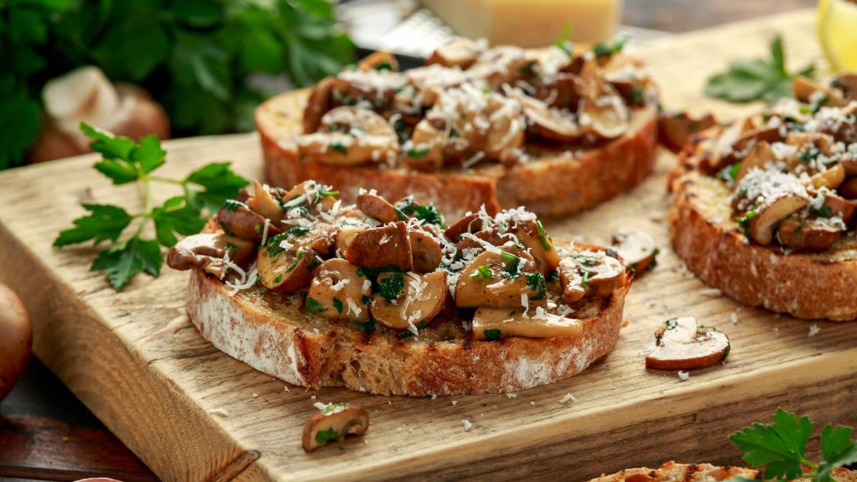Drei Pilzstullen mit Knoblauchfrischkäse, Petersilie und Parmesan auf einem Brett.