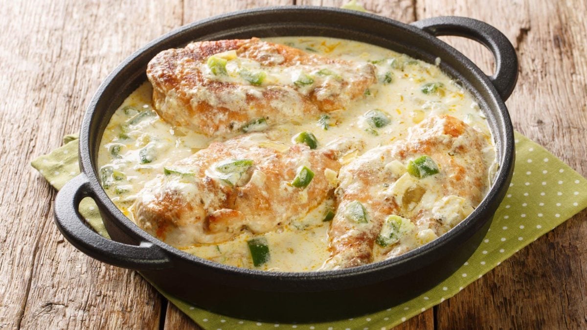 Pollo con crema in einer Gusspfanne auf gelber Serviette und Holztisch. Draufsicht.
