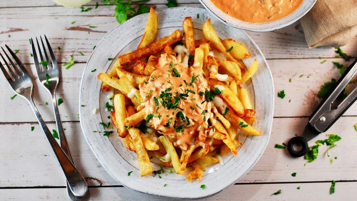 Ein Teller Poutine mit veganer Bratensauce und Petersilie, daneben zwei Gabeln, alles Draufsicht.