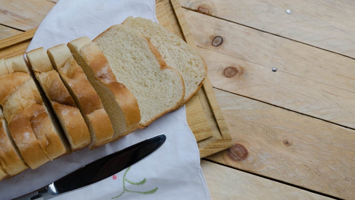 Selbst gemachtes Toastbrot aufgeschnitten auf Holzbrett und Holztisch. Daneben Buttermesser. Draufsicht.