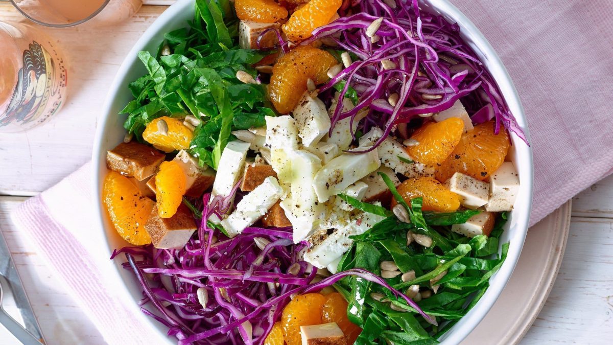 Spinat-Salat mit Ziegenkäse und Mandarinen in einer weißen Schüssel vor hellem Hintergrund in der Draufsicht.