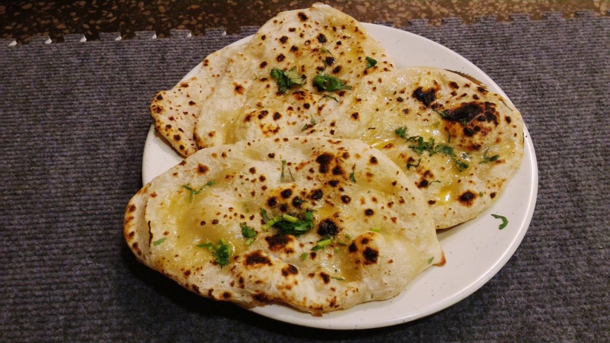 Stuffed Flatbread mit Käse und Kräuterbutter auf weißem Teller und dunklem Untergrund. Draufsicht.