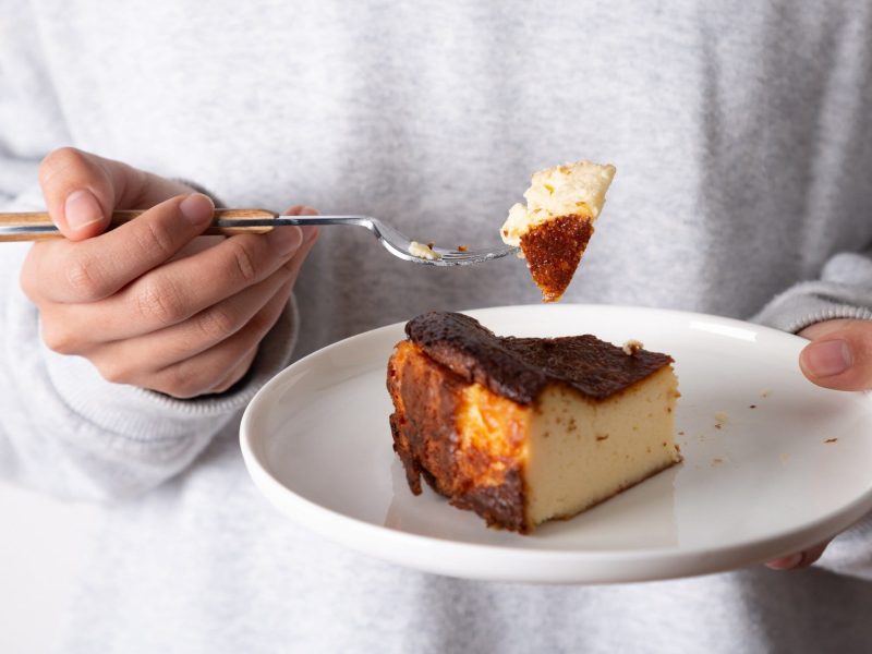 Unterschied zwischen Cheesecake und Käsekuchen: Eine Frau hält einen Teller mit Käsekuchen in der Hand, in der anderen eine Gabel mit einem Stück Kuchen.