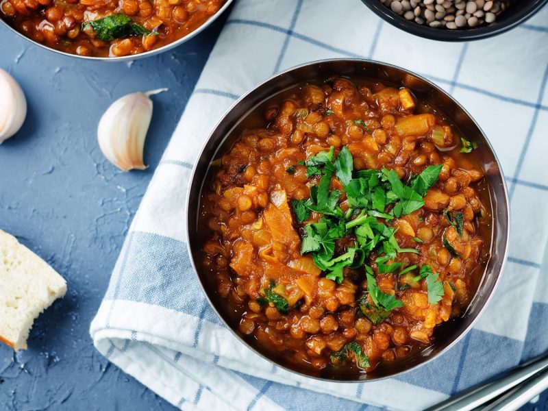 Eine Schüssel veganer Linseneintopf mit Petersilie in der Draufsicht, daneben Knoblauch und Brot.