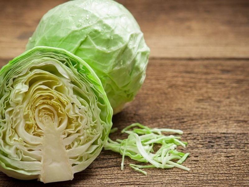 Frontalblick: Auf einem Holzbrette liegen ein ganzer Weißkohl und ein halber Weißkohl