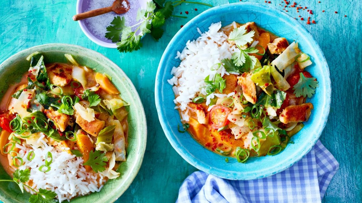 Draufsicht: Türkise Untergrund mit zwei Schüsseln gefüllt mit Reis und einem bunten Weißkohl-Hähnchen-Curry