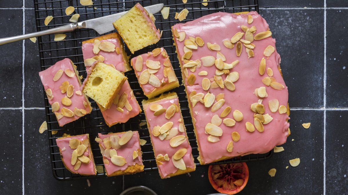 Zitronen-Ricotta-Kuchen mit Blutorangenglasur und Mandelblättchen angeschnitten auf einem Gitter in der Draufsicht.