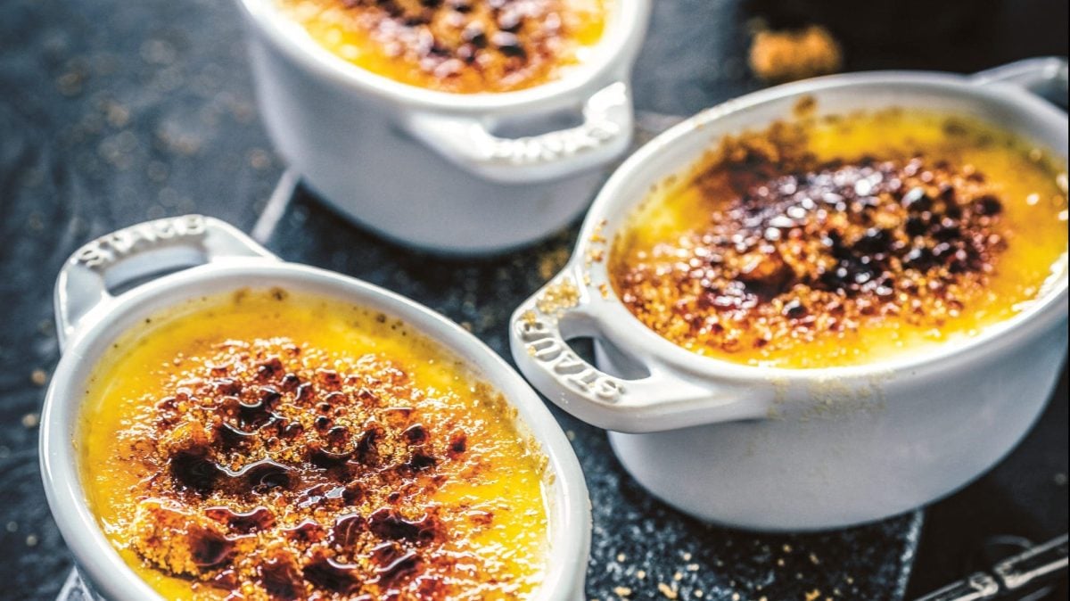 draufsicht schräg: drei kleine ofenbeste weiße formen mit einen überbackenen otangen pudding stehen auf einem dunklen Untergrund