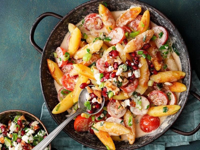 In einer Pfanne ist eine Portion Schupfnudeln mit Feta und Granatapfelkernen angerichtet. Das Gericht ist bunt und ausgefallen.