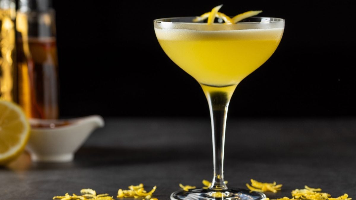 Ein Glas mit dem gelben Drink und etwas Zitronenschale.