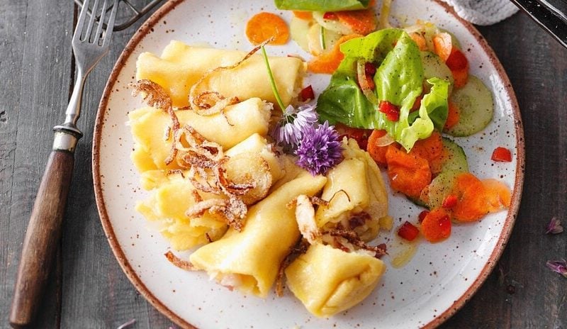 Allgäuer Krautkrapfen und Salat auf einem Teller, daneben eine Gabe, beides auf Holzhintergrund.