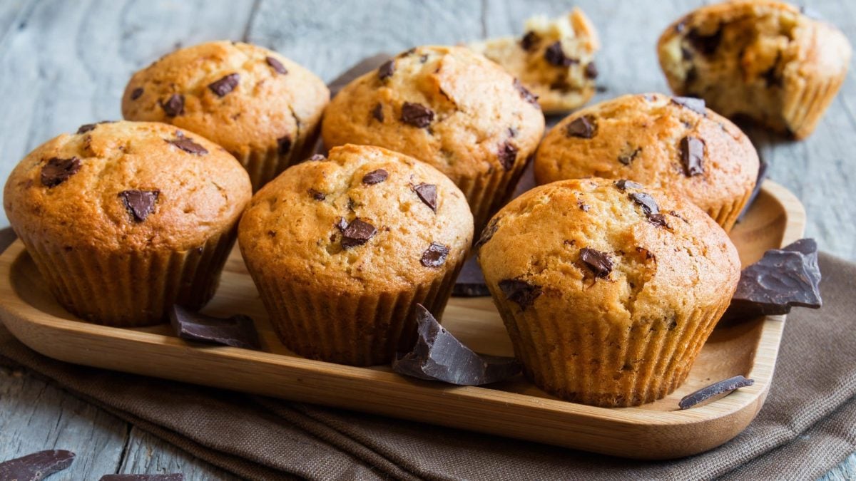 6 Bananenbrot-Muffins mit Schokodrops auf einem Holztablett, im Hintergrund noch ein Muffins.