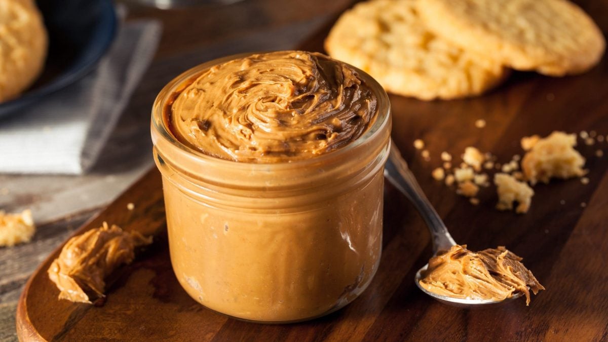 Ein Glas Biscoff-Creme, daneben ein Löffel mit der Creme, im Hintergrund Kekse.