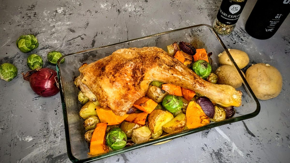 Eine Glas-Auflaufform mit dem Paprikagewürz-Hähnchen, Rosenkohl und Kürbis auf einem grauen Tisch.
