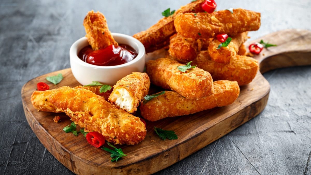 Chili-Halloumi-Fries mit roter Sauce in weißem Schälchen auf Holzbrett auf grauem Untergrund. Draufsicht.