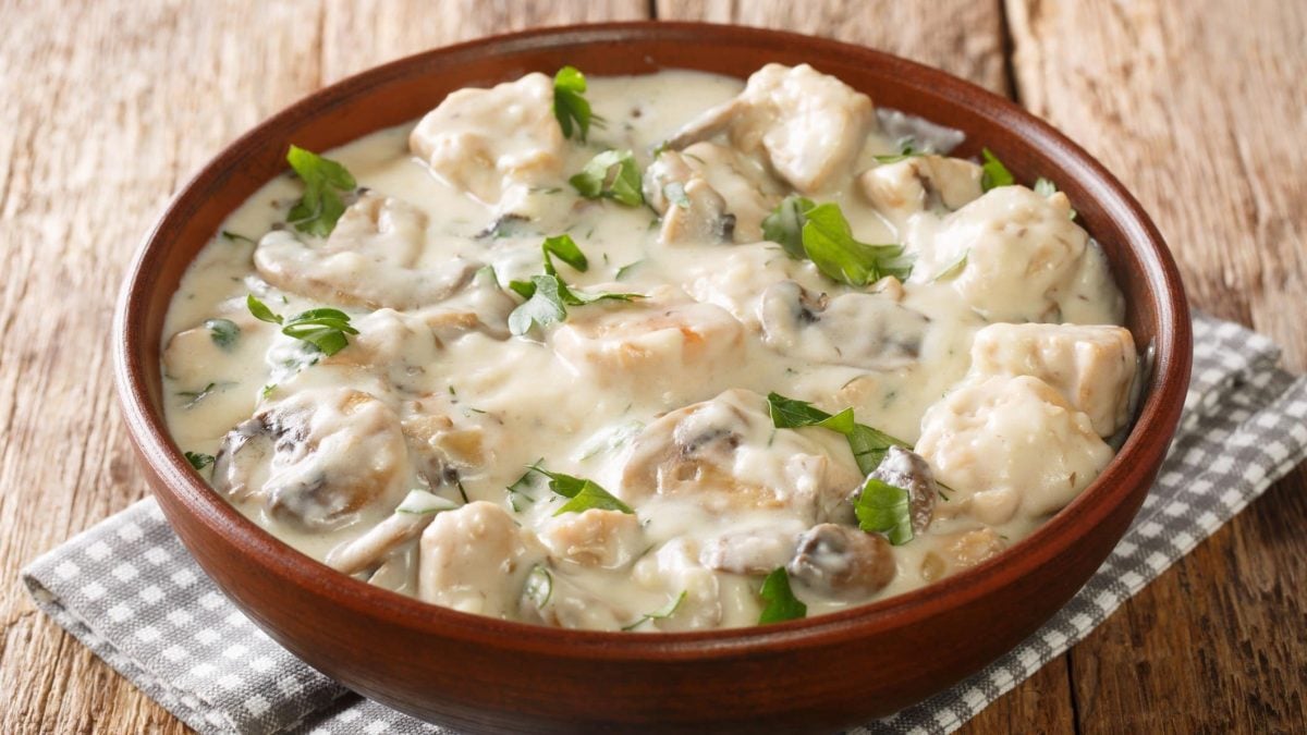Eine braune Schale mit dem Hähnchenragout auf einem Holztisch.
