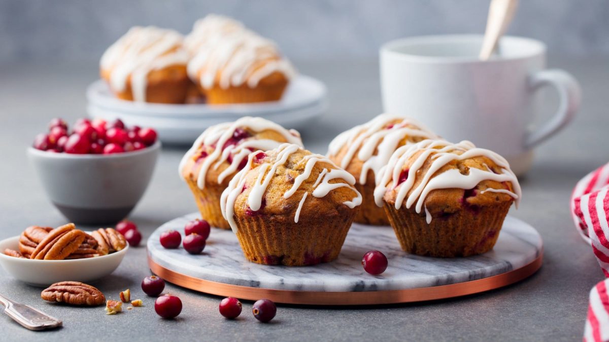 Cranberry-Muffins auf einem Marmor-Tablett, daneben eine Schale mit Cranberrys und Nüssen.
