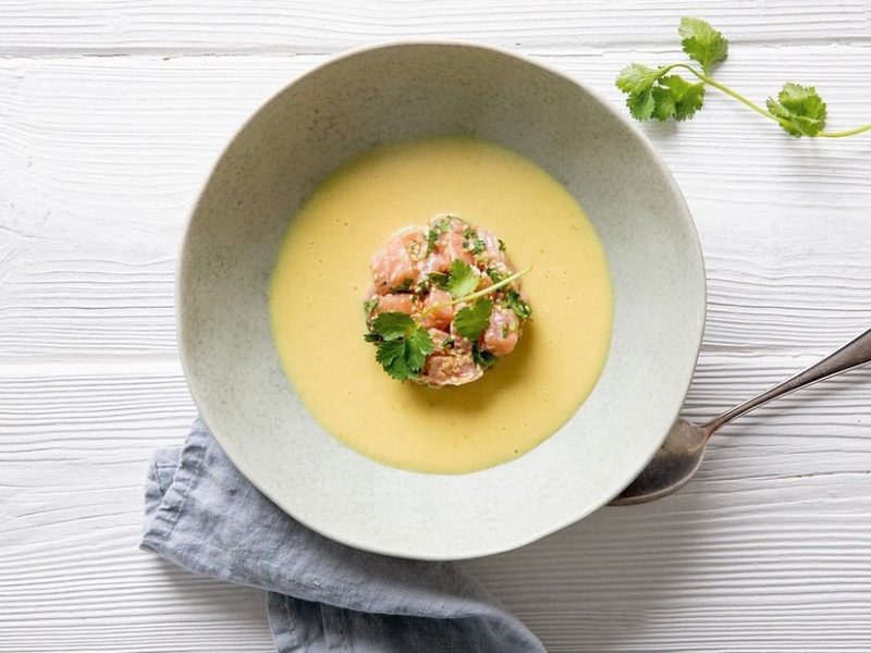 Currycremesuppe mit Lachstatar in weißem Teller vor hellem Hintergrund aus der Draufsicht.