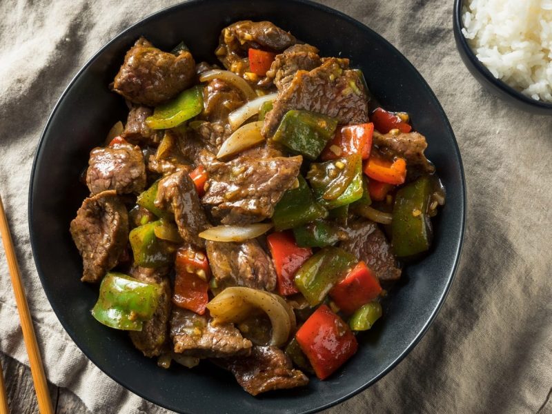Ein schwarzer Teller mit Cumin Beef auf einem gedeckten Tisch.