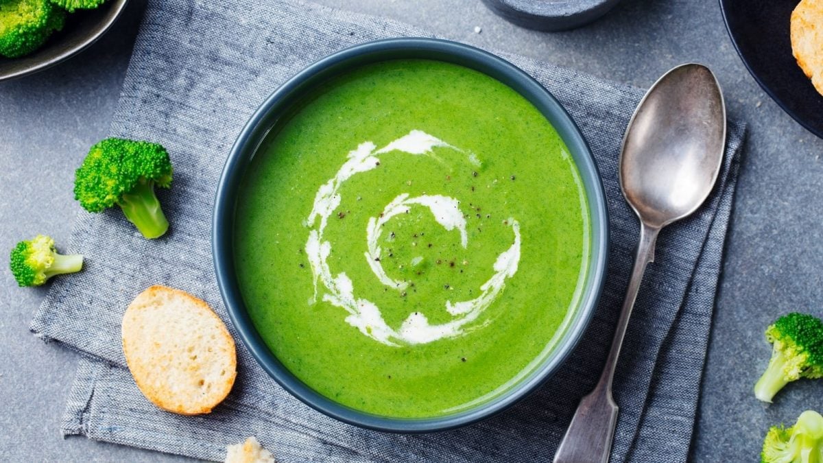 Eine Schüssel Green Goddess Suppe neben frischen Zutaten.