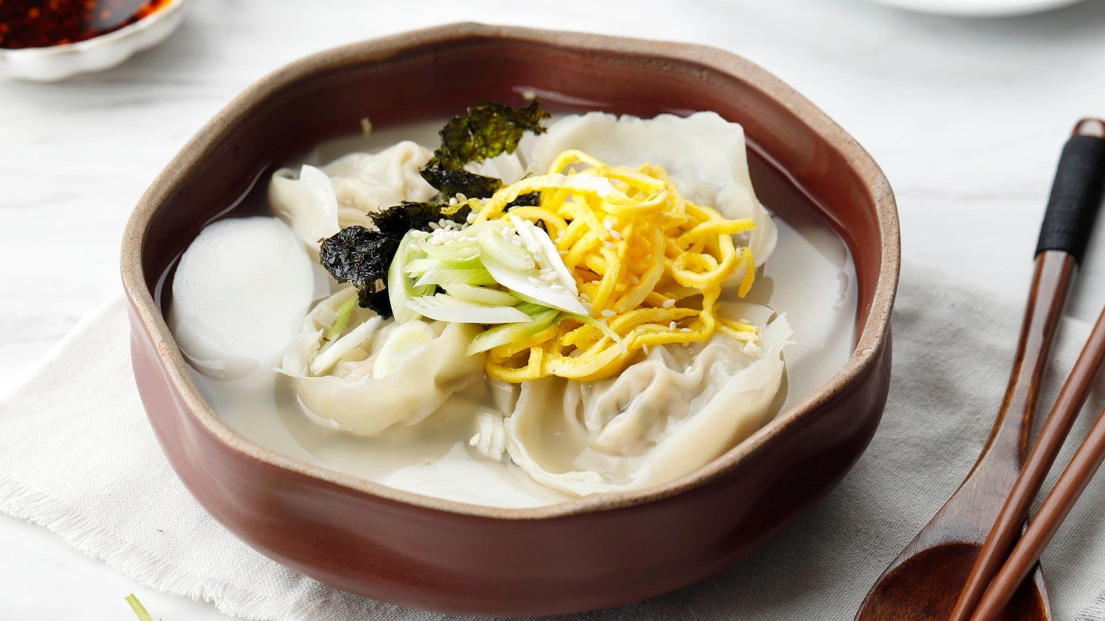 Eine Holzschüssel mit Mandu-Suppe auf einem weißen Tisch.