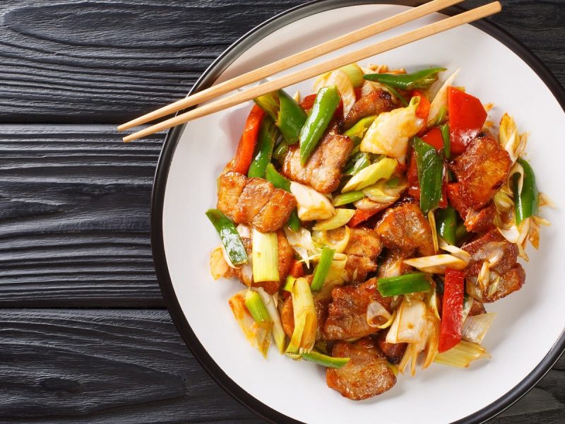 Ein weißer Teller mit Sichuan Schweinebauch auf einem schwarzen Tisch.