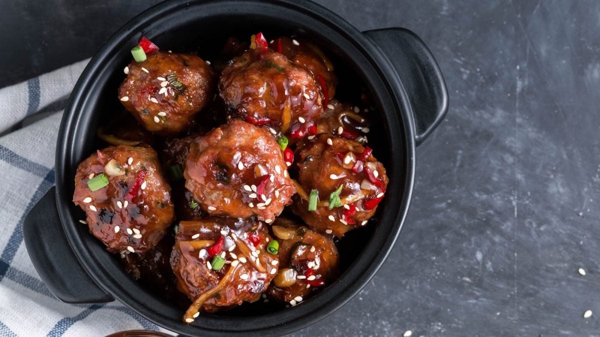 Ein schwarzer Topf mit Teriyaki-Hackbällchen auf einem weiß-blau karierten Geschirrtuch.