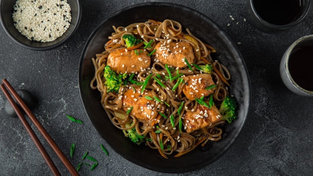 Ein schwarzer Teller mit Soba-Nudeln mit Teriyaki-Lachs.