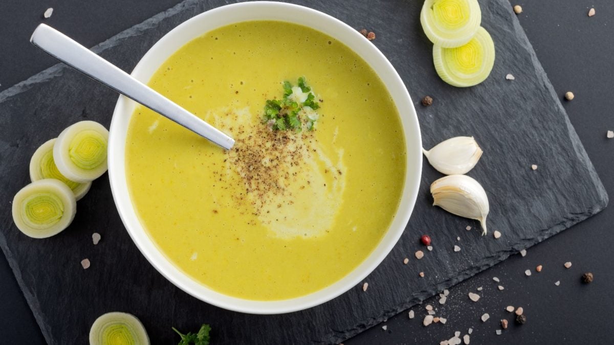 Eine weiße Schale mit der Lauchsuppe auf einer schwarzen Schiefertafel.