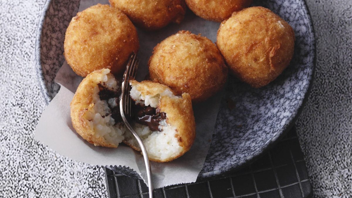 Frittierte Milchreisbällchen mit Schokoladenkern in einer Schüssel vor grauem Hintergrund.