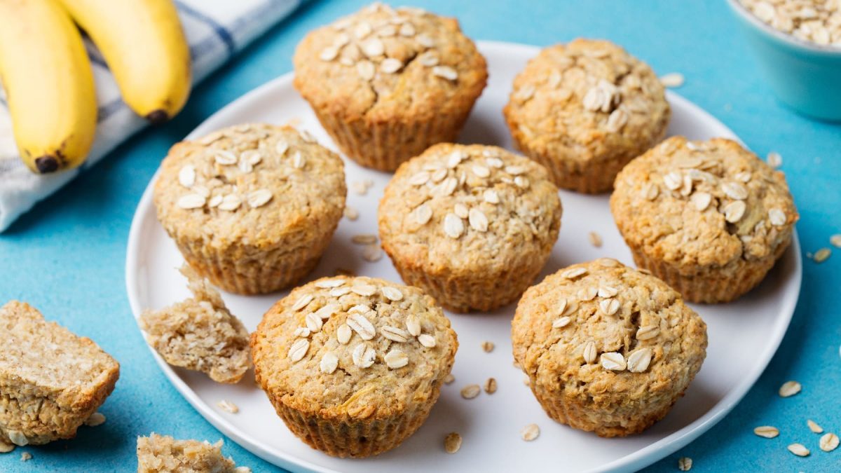 Mehrere Haferflocken-Muffins auf einem weißen Teller und blauem Untergrund.