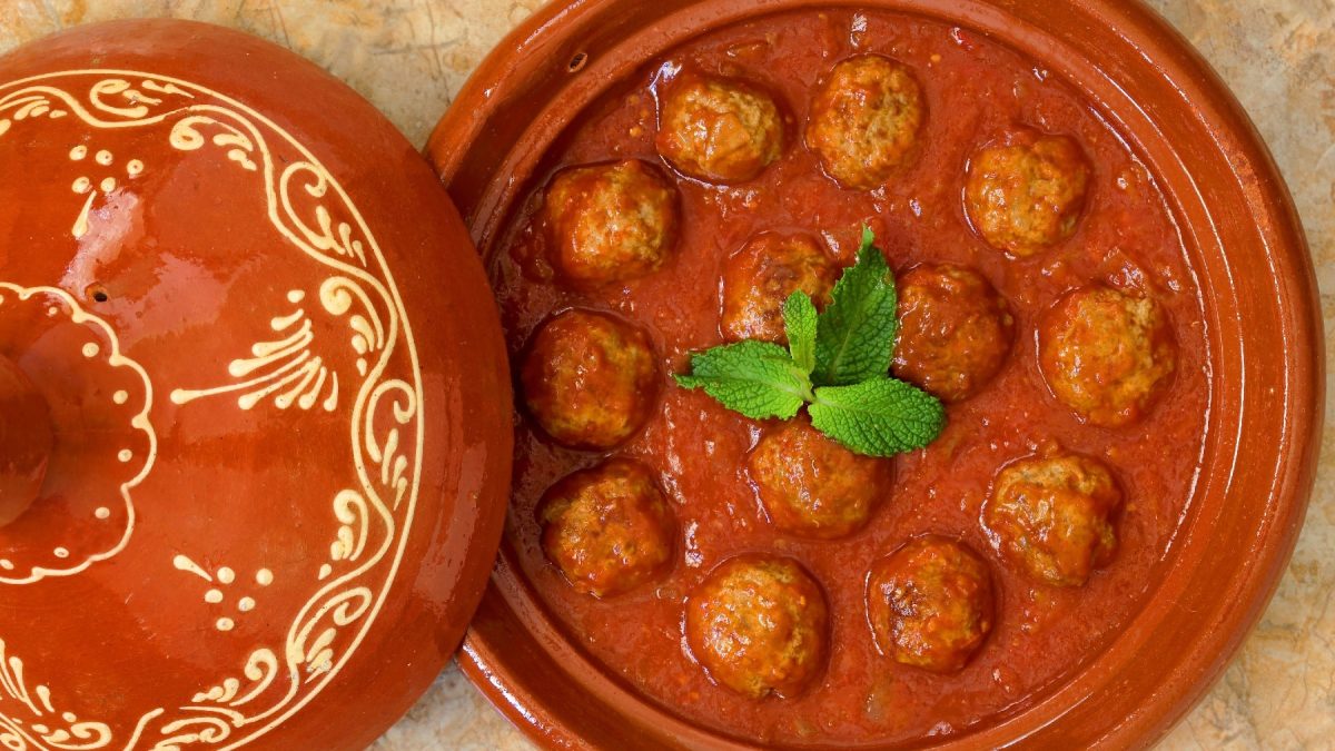 Marrokanische Fleischbällchen in einer Tomatensauce in einem Tontopf auf Marmorfliesen.
