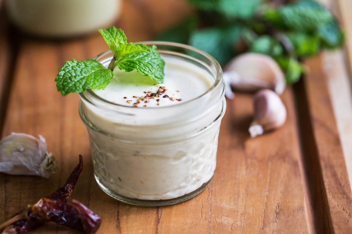 Ein Glas Knoblauch-Zitronen-Dressing, darin ein Blatt Minze.