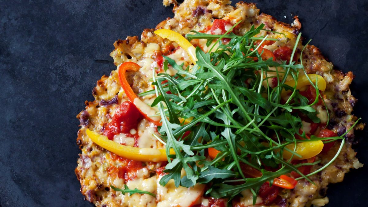 Eine kleine Schüttelpizza ind er NAhaufnahme von oben auf einem dunkelblauem Untergrund.