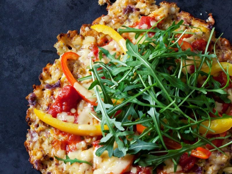 Eine kleine Schüttelpizza ind er NAhaufnahme von oben auf einem dunkelblauem Untergrund.