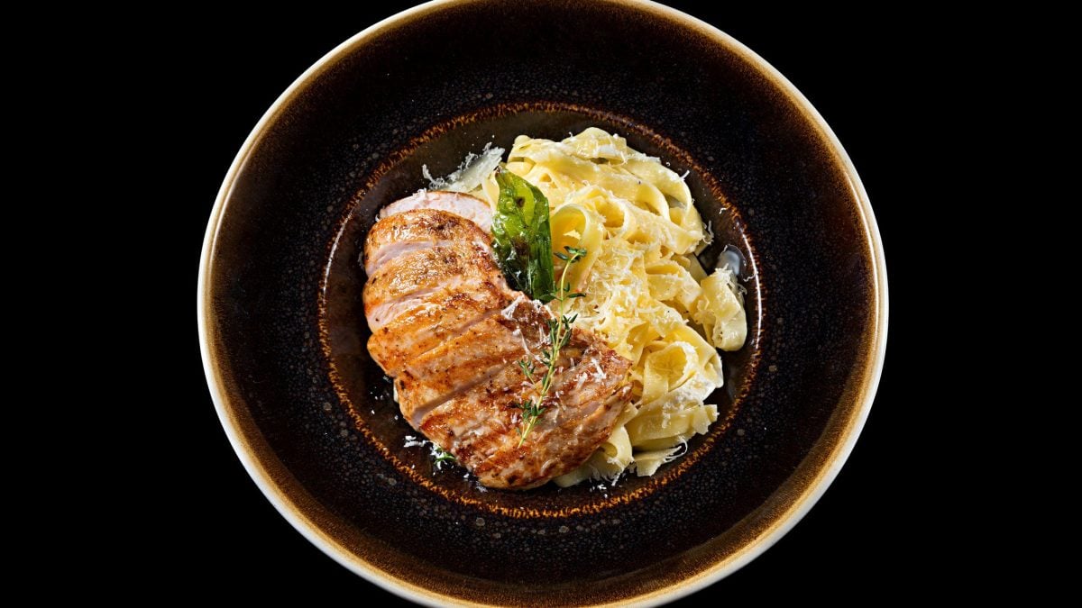 Pasta Chicken Alfredo auf dunklem Pastateller und dunklem Untergrund. Draufsicht.