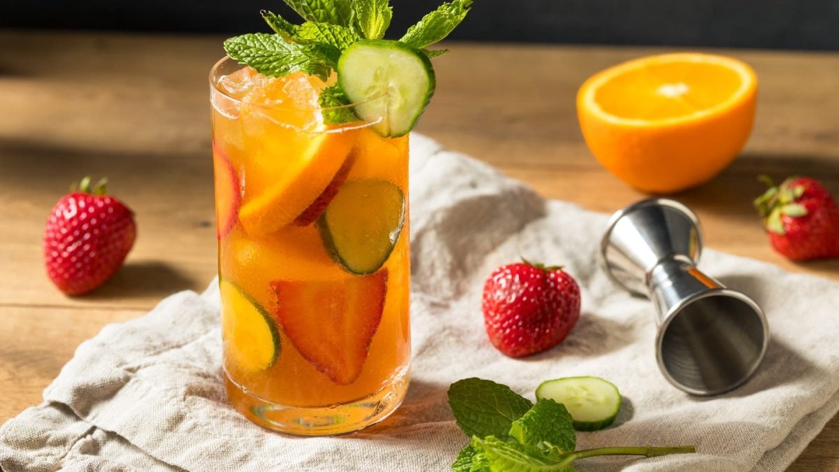 Ein Glas mit dem Pimm´s Cup auf einem dunklen Holztisch mit allerlei Fruchtdeko und Minze.