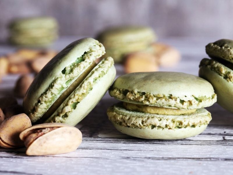 Pistazien-Macarons neben Pistazien vor hellem Hintergrund.