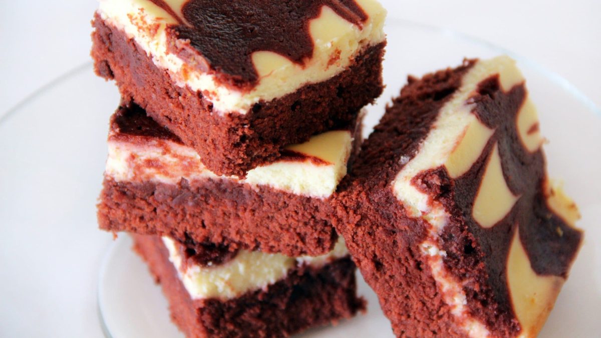 Red Velvet Brownies mit Vanilla-Icing gestapelt auf weißem Teller. Draufsicht.