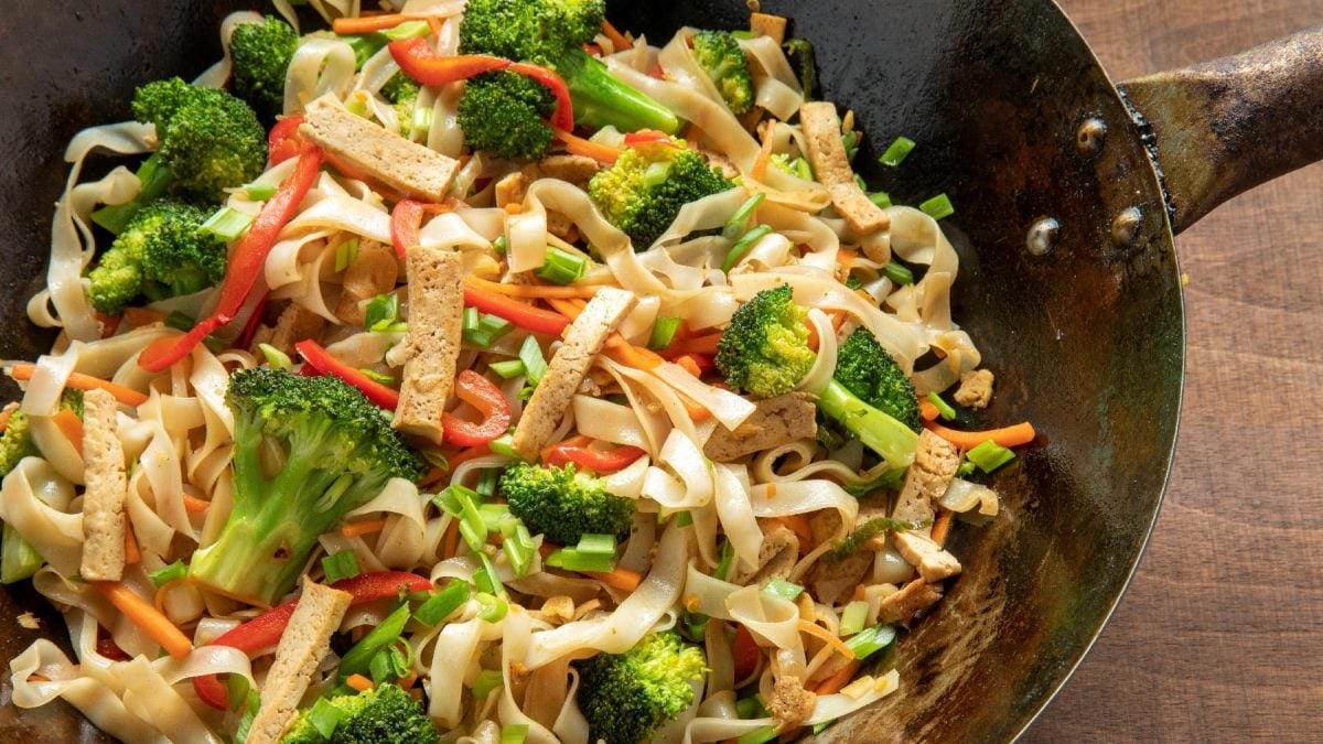 Ein schwarzer Wok mit dem Reisband-Nudelsalat auf einem dunklen Holztisch.