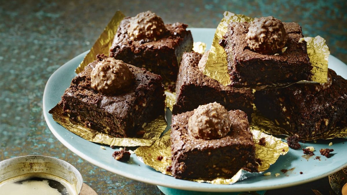 Rocher Brownies auf goldenem Pralinenpapier auf einem blauen Teller vor blauem Hintergrund.