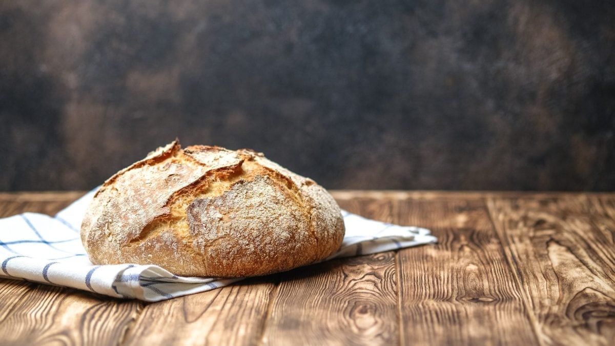 Selbst gebackenes Krustenbrot auf Tuch und Holztisch. Frontalansicht.